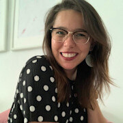 A woman with long brown hair wearing glasses and a black polka dot top smiles at the camera.